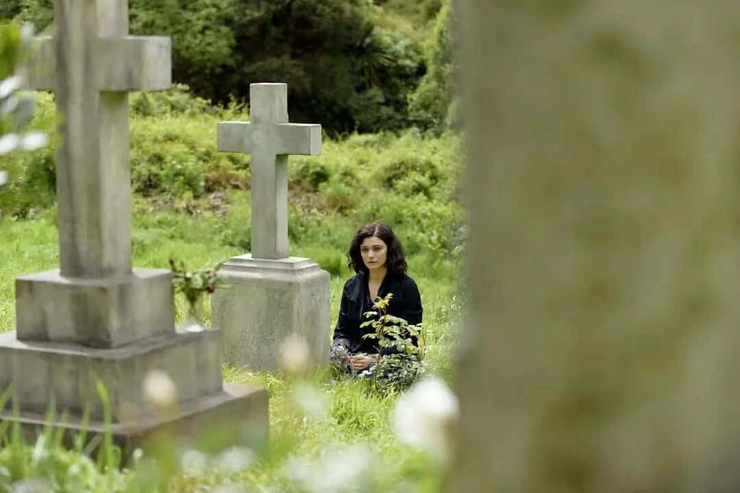 大洋之间的灯光-女主角在墓地中，手持花束坐在墓碑前沉思