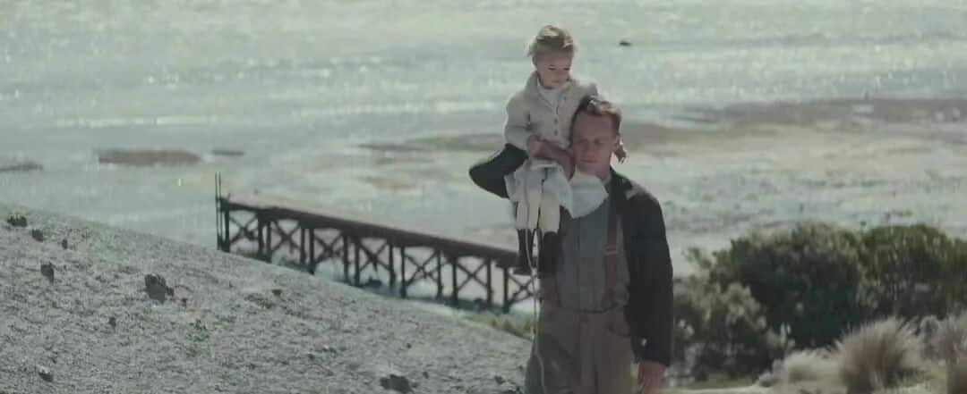 大洋之间的灯光-男主角肩上扛着女儿，两人在海边的沙滩上行走