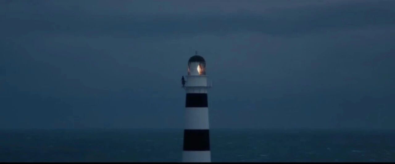 大洋之间的灯光-一座黑白相间的灯塔矗立在海边，灯光在夜色中闪烁