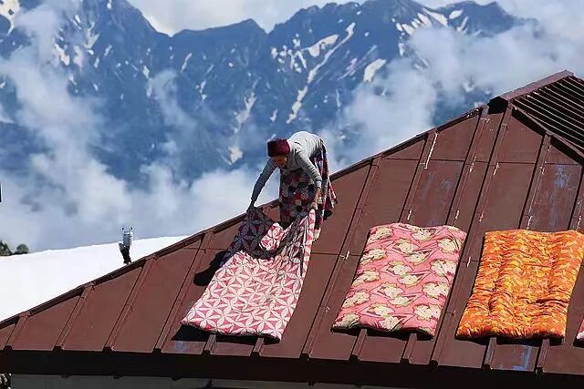背负春天-一位女性在屋顶上晾晒色彩鲜艳的地毯，背景是壮丽的雪山