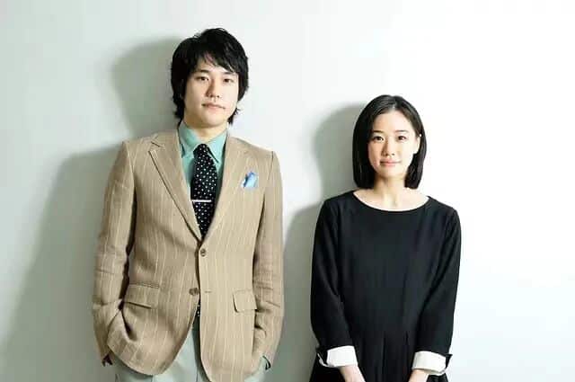 背负春天-男女主身着正式服装，站在白色背景前
