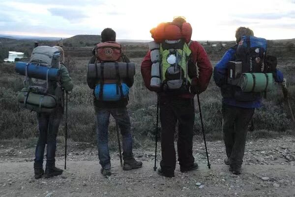 朝圣之路四位徒步旅行者背负行囊，站在开阔的自然景观中