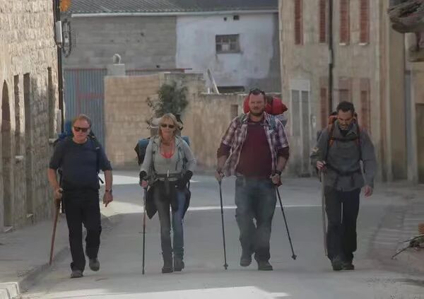 朝圣之路四位徒步旅行者手持登山杖沿着城市街道行走