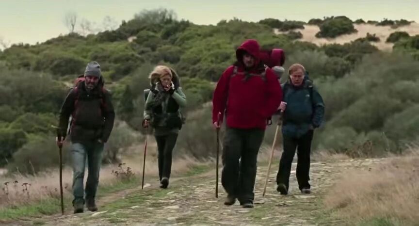 朝圣之路四位朝圣者全副装备，背负行囊，手持登山杖，坚定地行走在乡间小路上